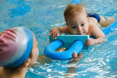 Early age swimming in pool. baby boy trained to swim in water coach woman in indoor swimming pool  