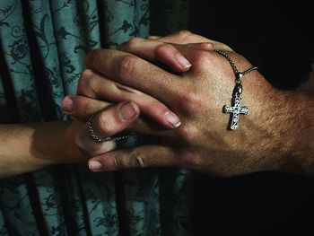 Cropped image of couple holding hands with cross
