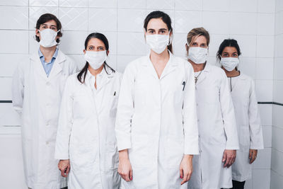 A group of five doctors with a mask on their face and a white coat standing up in a hospital room