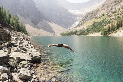 Side view of man diving in lake against mountains at banff national park