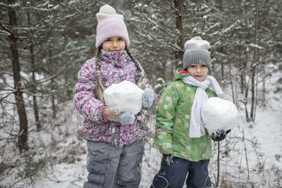 Portrait of cute sibling holding snow ball during winter