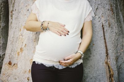 Midsection of pregnant woman standing against tree