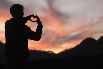 Silhouette man photographing against sky during sunset