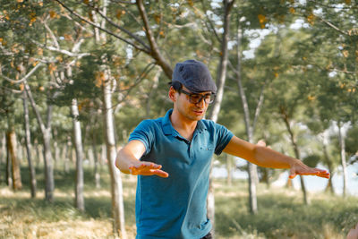 Mature man wearing cap and eyeglasses standing against trees in forest