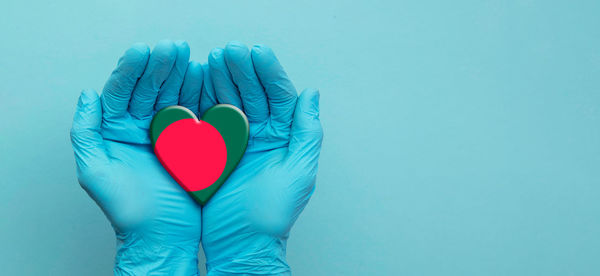 Midsection of woman holding heart shape against blue background