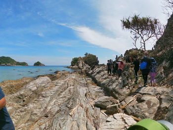 People on rock by sea against sky