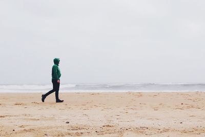 Man walking on shore at beach against sky