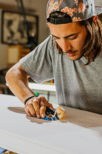 Focused male master using hand plane and shaping smooth surface of surfboard in workshop