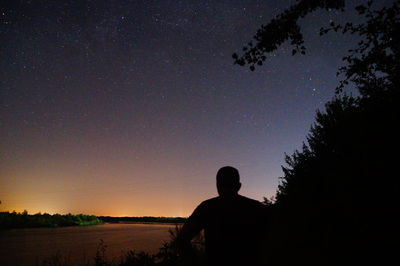 Rear view of silhouette man standing against sky at night