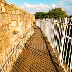 Footpath by wall against sky