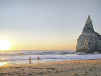 People walking on beach against clear sky during sunset