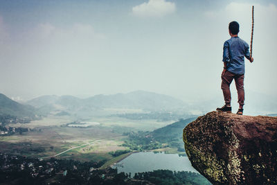 Rear view of man standing on rock against landscape