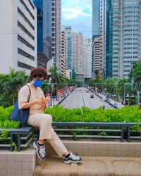 Man sitting on bench against buildings in city