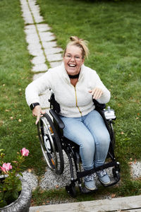 Full length portrait of smiling disabled woman sitting on wheelchair in yard