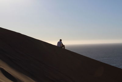 Man sitting on beach against sky during sunset