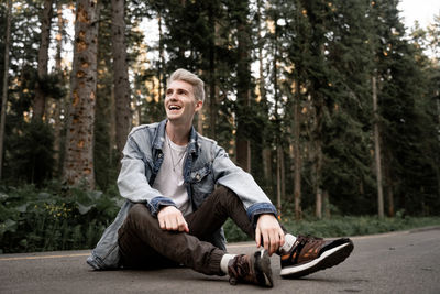 Cheerful young man sitting on road in forest