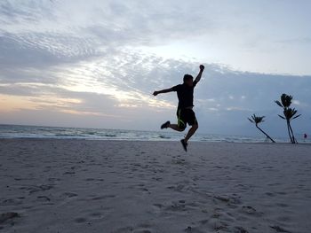 Full length of man jumping on beach against sky