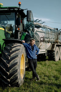 Happy mature farmer standing by tractor on field