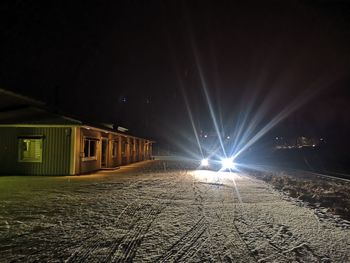 Illuminated street amidst buildings against sky at night