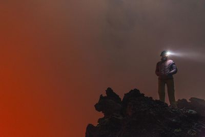 Woman with head torch standing against orange sky