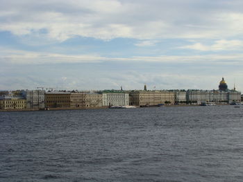 View of buildings by river against cloudy sky