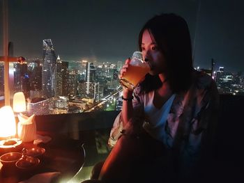 Woman sitting by illuminated buildings in city at night