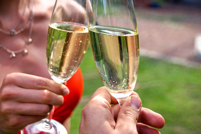 Cropped hands of friends toasting champagne flutes in yard