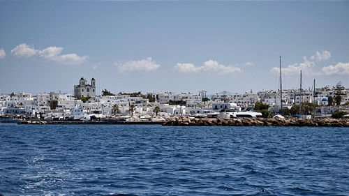 Sailboats in sea by buildings against sky