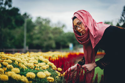 Portrait of young woman by flowers at park