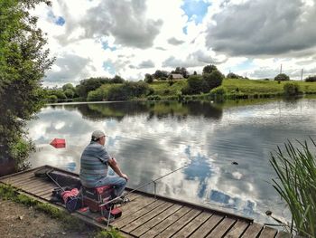 Rear view of men sitting on lake against sky