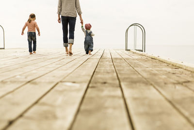 Rear view of family walking on pier against clear sky