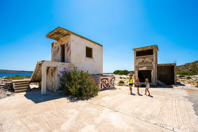 Rear view of man standing by building against clear blue sky