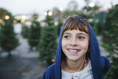 Close-up of happy girl looking away while standing by pine tree at farm during christmas