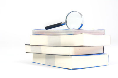 Close-up of magnifying glass on stacked books against white background