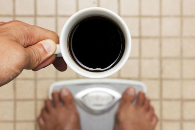 Low section of man holding black coffee while standing on weight scale