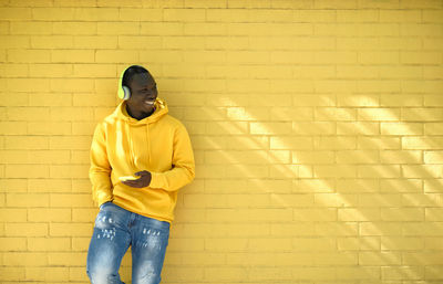 Young man listening music against yellow wall