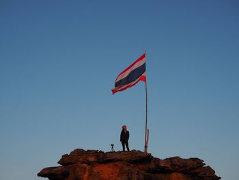 Low angle view of man standing on rock against clear blue sky