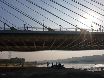 People on suspension bridge over river against sky