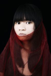 Close-up portrait of young woman with red textile against black background