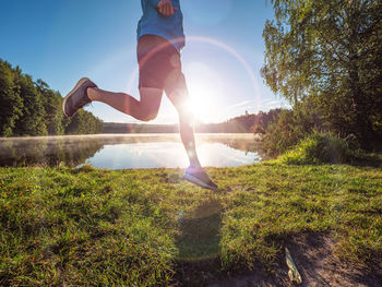 Athlete at the lake running against sunrise and colorful nature.