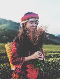 Woman wearing traditional clothing holding flowers against sky