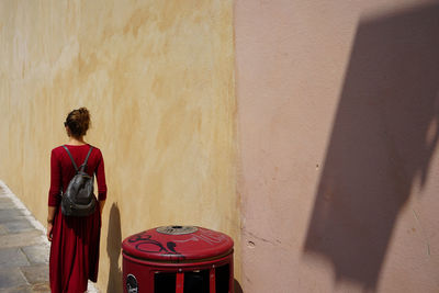 Rear view of woman in red dress walking by wall