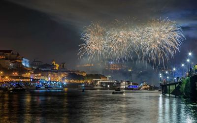 Firework display over river in city against sky at night