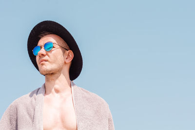 Young man wearing sunglasses and hat against clear blue sky