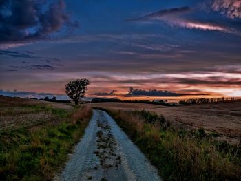 Road passing through field against cloudy sky