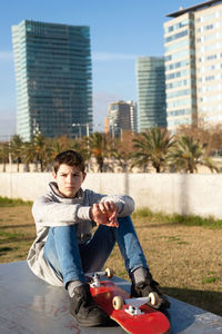 Serious teen sitting on skatepark ramp with a skateboard, looking away