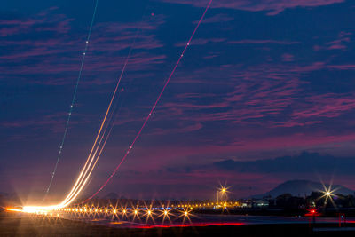 Light trails at airport runway against cloudy blue sky at dusk