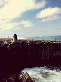 Bride and bridegroom standing by sea on cliff