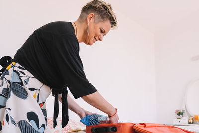 Smiling woman packing suitcase at home