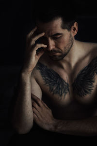 Shirtless man with tattoo on chest against black background